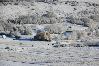 A building situated in a snowy field with hay bales, surrounded by frost-covered trees and rolling hills in the background