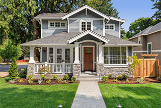 A two-story craftsman home with blue-grey siding, white trim, and stone accents features a stone paver walkway leading through a manicured green lawn to the front door