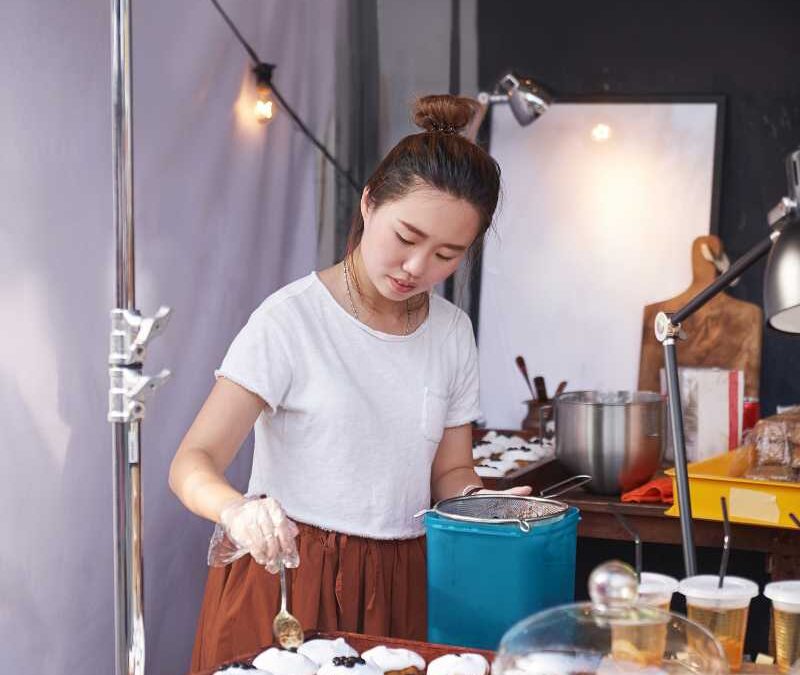 A woman in a white t-shirt decorates pastries with icing on a wooden tray