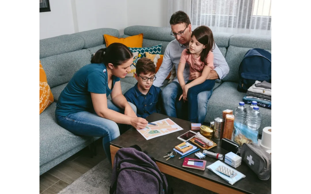 A family of four sits around a coffee table packed with emergency supplies, looking at a map together as they plan a survival or evacuation strategy - www.turnerhouserins.com